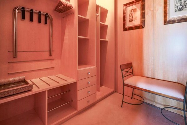 Un vestidor rosa con estantes abiertos, cajones y un banco.