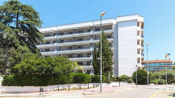 Un immeuble résidentiel à plusieurs étages, doté de balcons, entouré de verdure et surplombant un ciel dégagé.