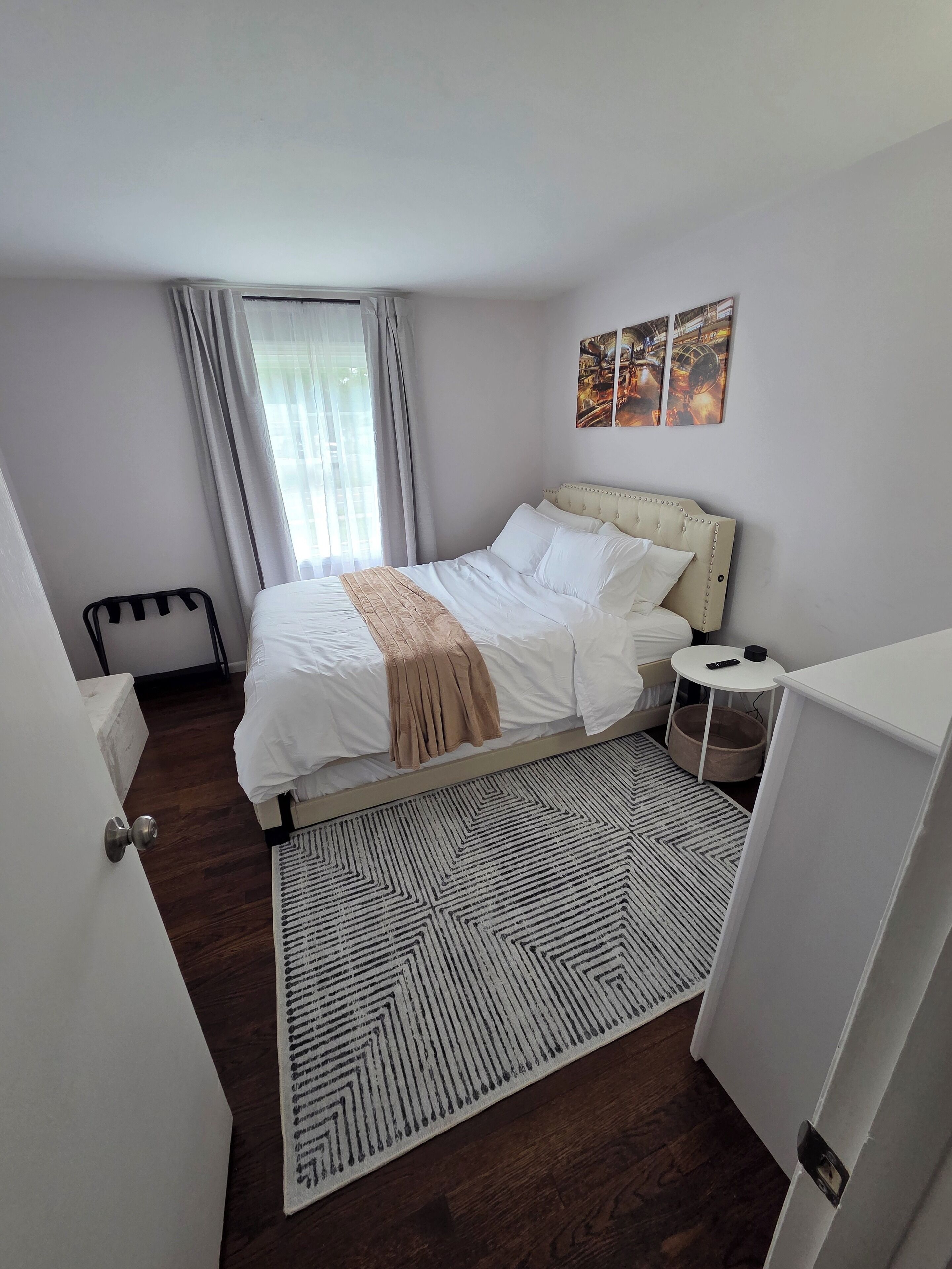 Una camera da letto con un letto, un comodino, un tappeto e una finestra con tende.