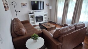 A modern living room with a brown leather sofa, a white coffee table, and a fireplace. - Welcome to The Hangar, a newly remodeled travel-themed stay, 4 minutes from BDL. (Windsor Locks)