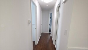 A narrow hallway with wooden flooring and white walls, leading to a door at the end. - Welcome to The Hangar, a newly remodeled travel-themed stay, 4 minutes from BDL. (Windsor Locks)