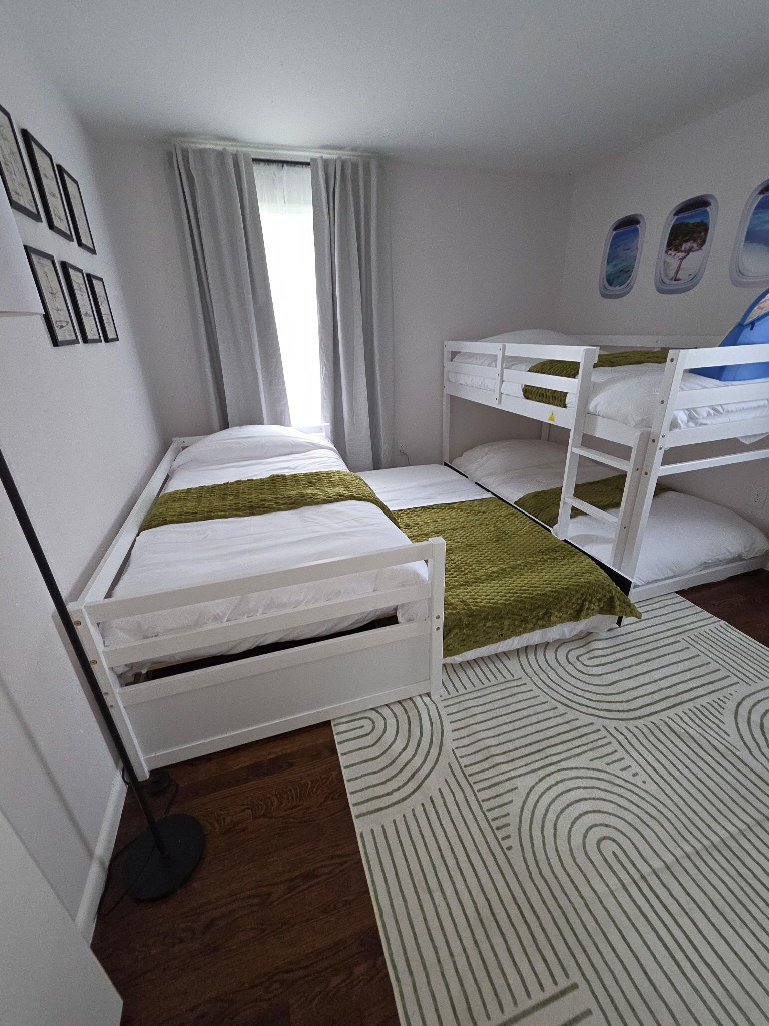 A room with two bunk beds, a window with curtains, a patterned rug, and framed pictures on the wall.