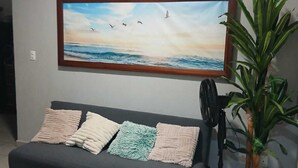 Un salon avec un canapé gris foncé, un tableau représentant un paysage marin, une plante en pot et une petite table blanche.