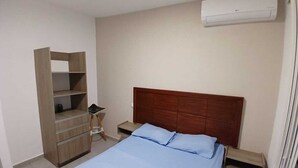 Une chambre à coucher comprenant un lit, une armoire en bois, une table de chevet et un appareil de climatisation.