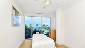Ein Hotelzimmer mit Bett, Holzschrank und großem Fenster mit Blick auf Palmen und Strand.