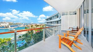 Ein Balkon mit Blick auf einen Yachthafen und einen Strand, mit Holzstühlen und einer Glasreling.