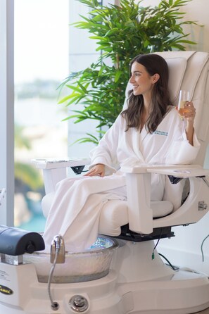 A person in a white robe sitting in a massage chair with a glass of drink, a plant, and a window in the background. - Margaritaville Waterpark One Bedroom Oceanfront Residence with Kitchen and. (Nassau)