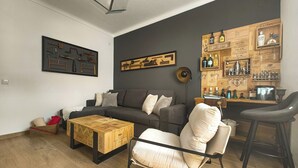 Ein modernes Wohnzimmer mit einem dunkelgrauen Sofa, einem Holztisch und einer Bar mit verschiedenen Flaschen und Gläsern.
