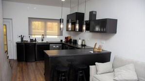 Et moderne køkken med sorte skabe, en central ø med barstole, og en hvid sofa i opholdsstuen.