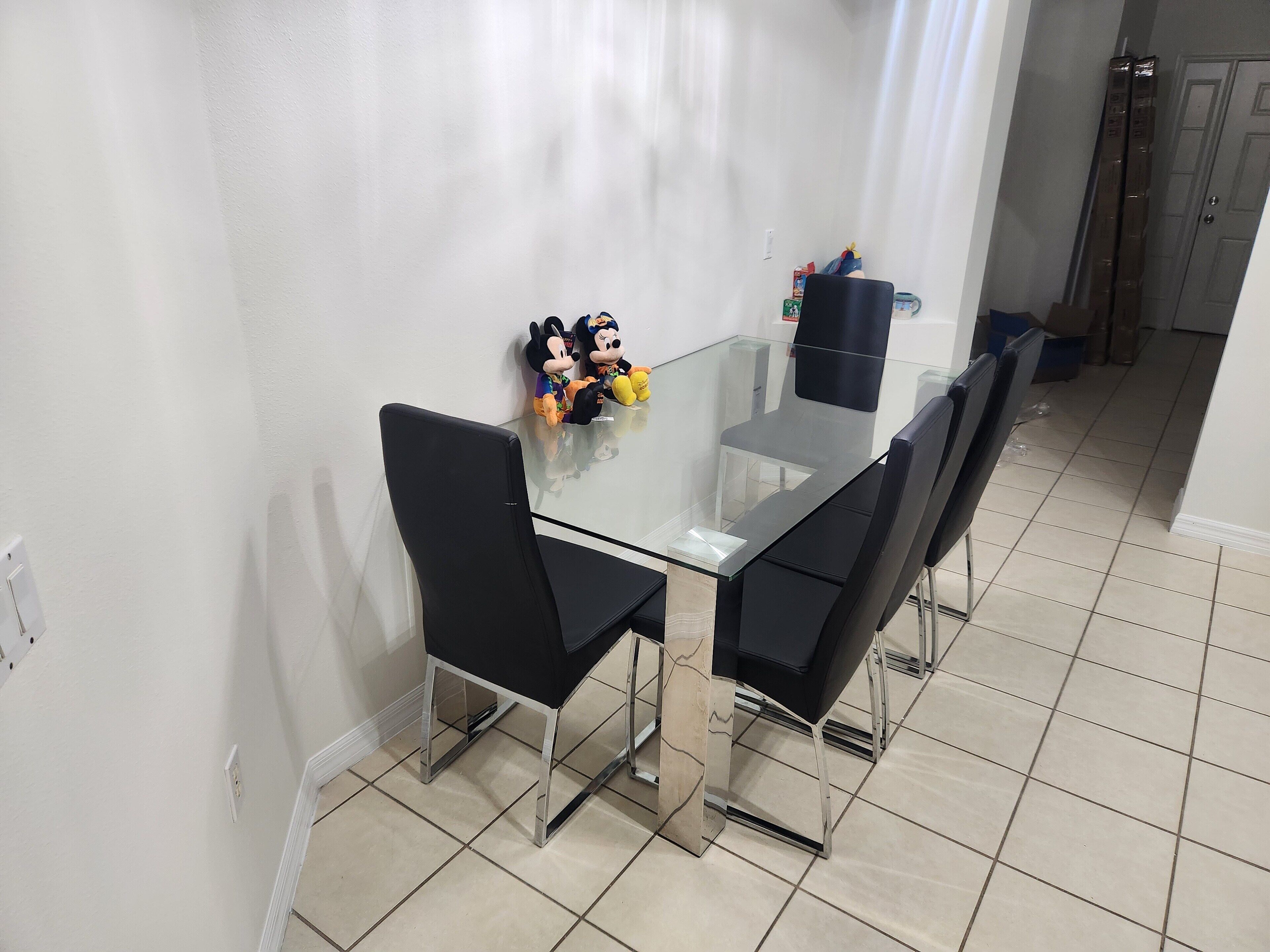 A dining area with a glass-top table, black chairs, and Mickey and Minnie Mouse figurines.