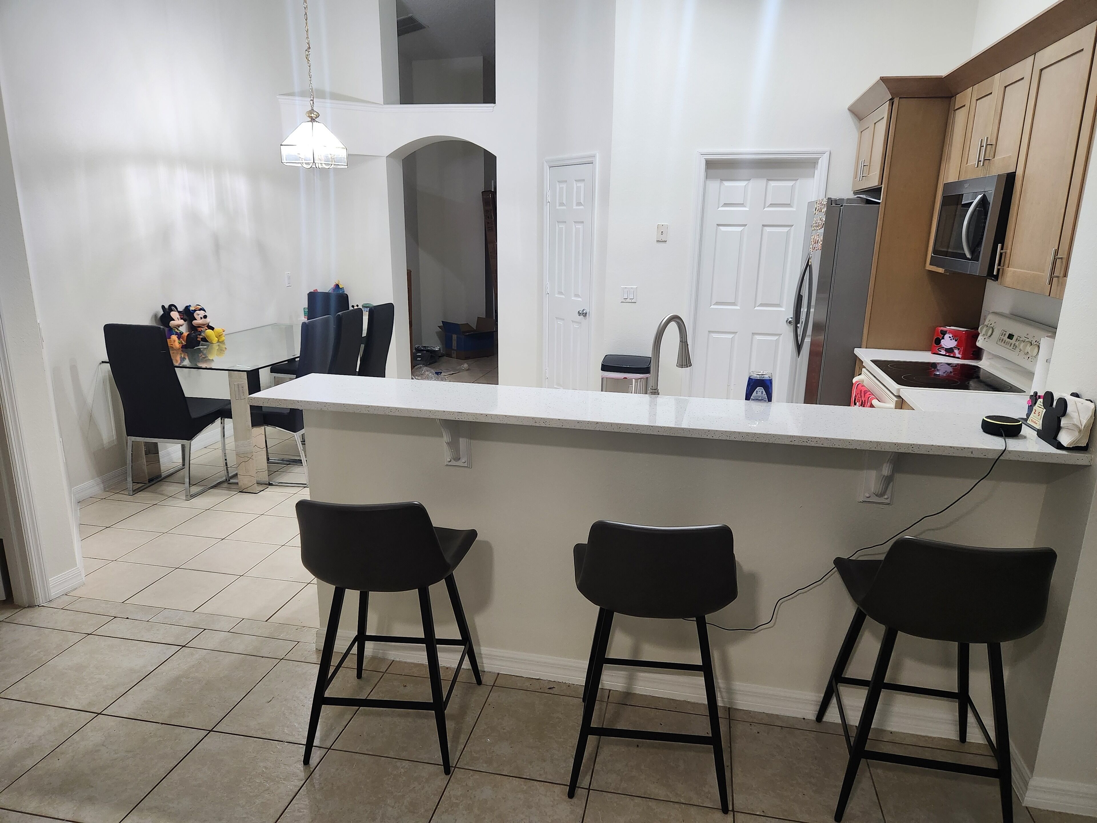 A modern kitchen with a central island, black bar stools, a dining area with chairs, and a visible microwave.