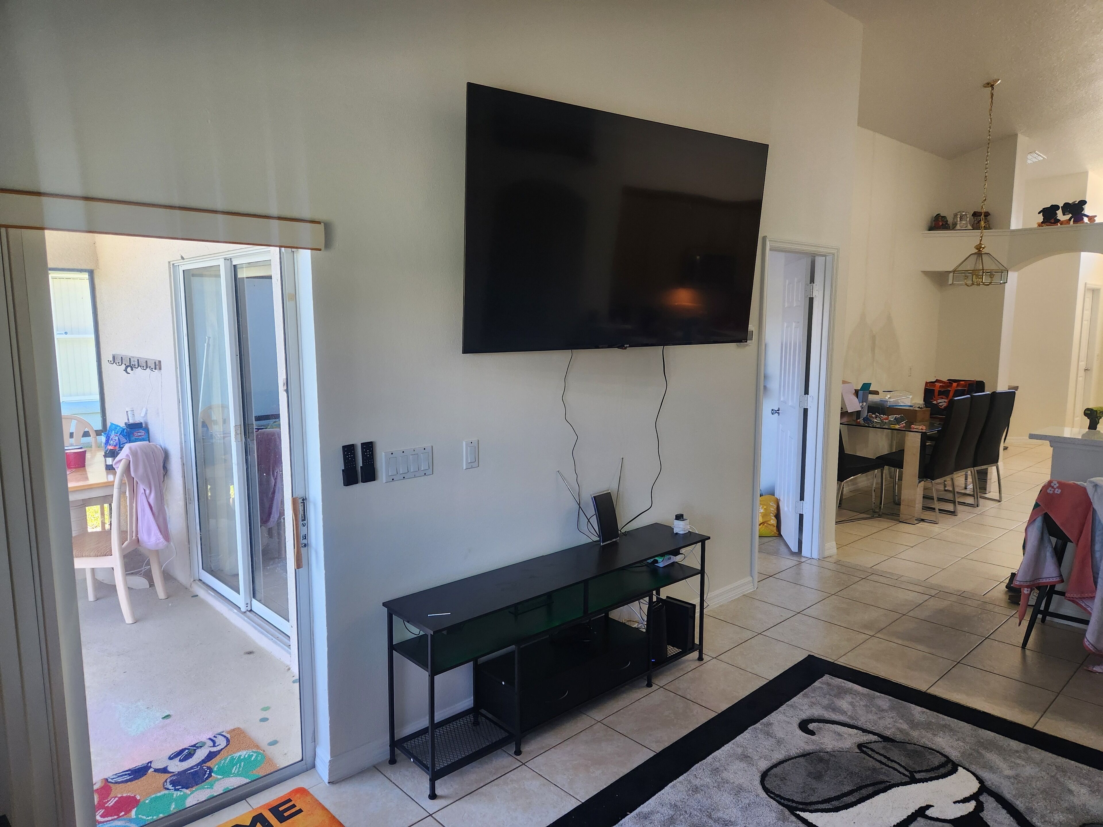Ein Wohnzimmer mit Wand-Fernseher, Glastür zum Balkon und Essbereich mit Stühlen und Tisch.