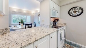 Uma cozinha moderna com armários brancos, bancada de mármore e micro-ondas embutido.