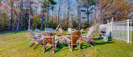 A backyard with a wooden table and chairs, surrounded by trees and a white fence.