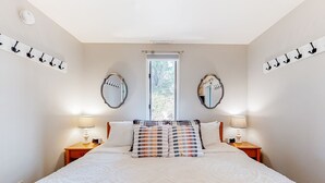 Quarto com uma cama grande, duas mesas de cabeceira com luminárias, uma janela com vista e dois espelhos fixados na parede.