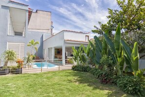 Propiedad residencial con piscina, terraza techada y jardín cuidado con diversas plantas.
