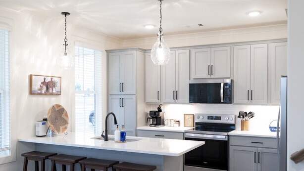 Una cocina moderna con armarios blancos, una isla central con taburetes de bar, electrodomésticos de acero inoxidable e iluminación colgante.