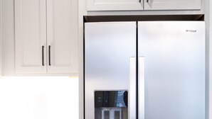 Un refrigerador Whirlpool de acero inoxidable con dispensador de agua, muebles de cocina blancos y piso de madera.