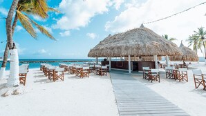 Un resort frente a la playa con estructuras de techo de paja, sillas de descanso blancas y un paseo de madera.