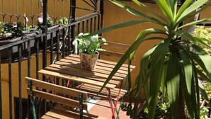 Un balcón con mesa de madera, plantas en macetas y faroles colgantes.