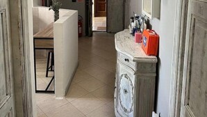 Un pasillo con piso de baldosas de mármol, un tocador blanco con espejo y una puerta con letrero verde de salida de emergencia.