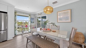 A modern kitchen with a glass dining table, wooden chairs, and a hanging light fixture.