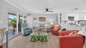 A spacious living room with a balcony, a kitchen with white cabinets, and a ceiling fan.