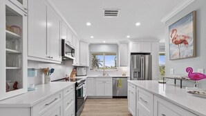 A modern kitchen with white cabinetry, stainless steel appliances, and a view of palm trees outside.