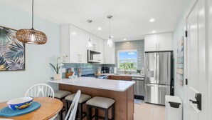 Una cocina moderna con armarios blancos, una isla grande, electrodomésticos de acero inoxidable y vistas al exterior.