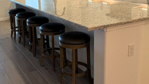 Una cocina con encimera de granito, pileta de acero inoxidable y taburetes de madera.