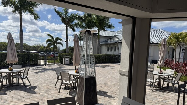 Un área de patio al aire libre con mesas, sillas, palmeras y sombrillas.