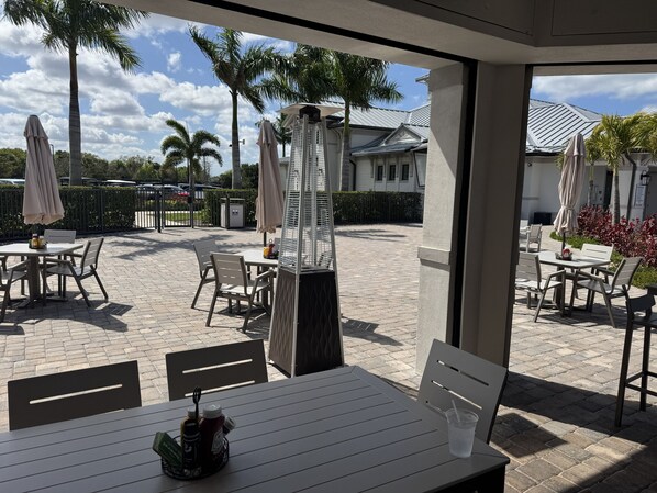 An outdoor patio area with tables and chairs, palm trees, and umbrellas.
