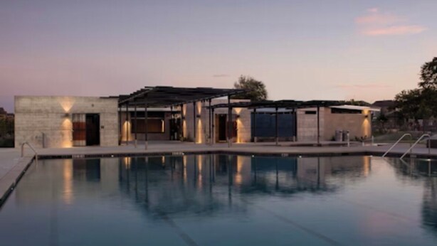 Un bâtiment moderne avec une piscine à l’avant, doté d’un espace extérieur couvert et offrant une vue sur un ciel dégagé.