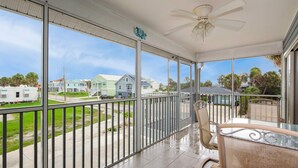 A spacious balcony with a glass table and chairs, a ceiling fan, and a view of a residential area with houses and a street. - Beach Villa (Fort Myers Beach)