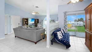 A spacious living room with a grey sofa, a television, and a balcony with a view of the outside. - Beach Villa (Fort Myers Beach)
