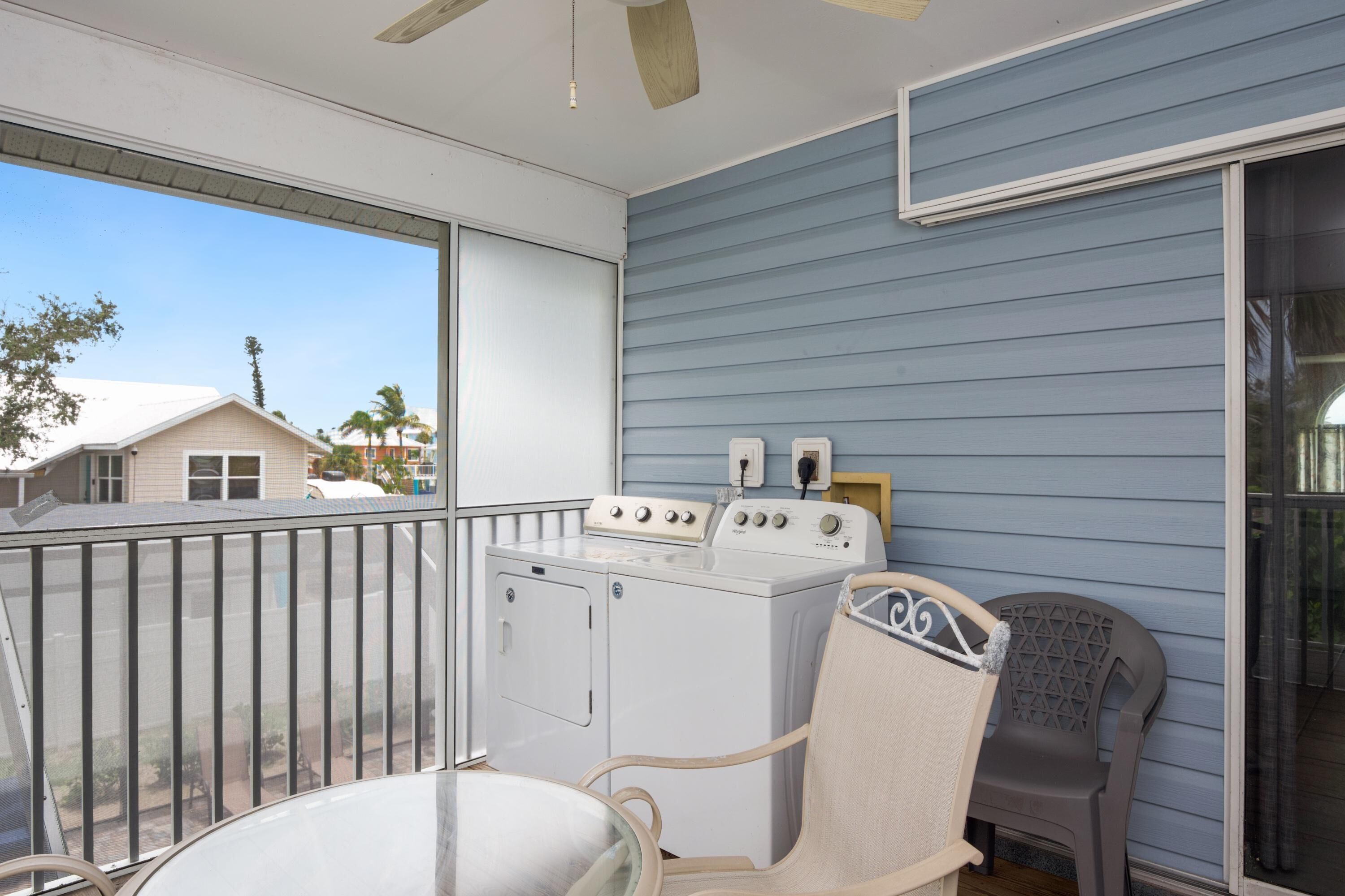 A balcony with a washing machine, a chair, and a view of neighboring houses.