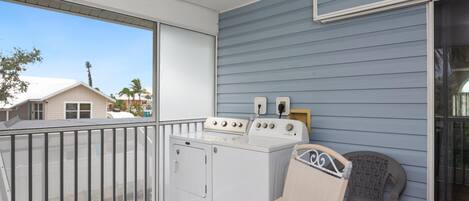 A balcony with a washing machine, a chair, and a view of neighboring houses.