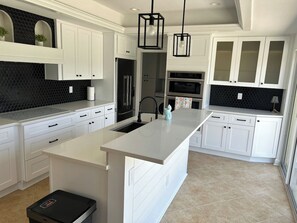 Een moderne keuken met witte kasten, een centraal eiland en een zwarte backsplash van hexagonen.