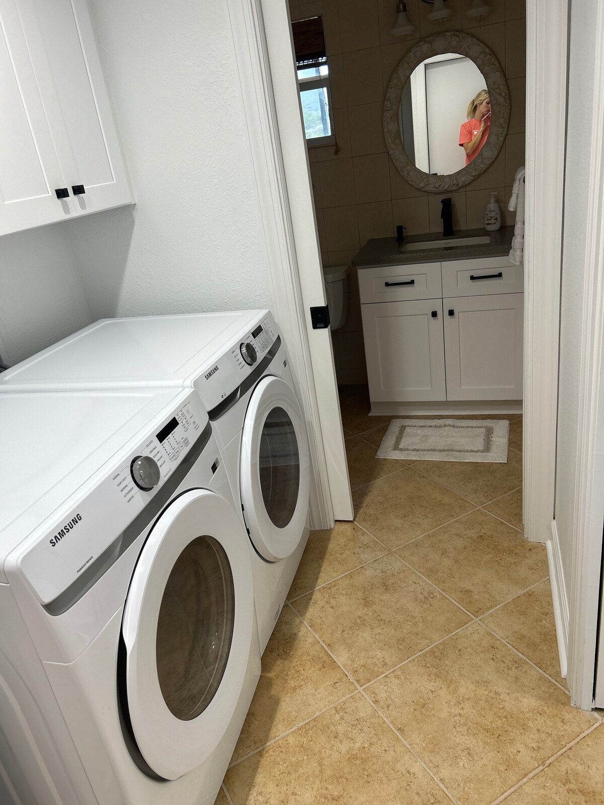 A laundry area with a Samsung washing machine and dryer, a mirror, and a small countertop with a sink and toiletries.