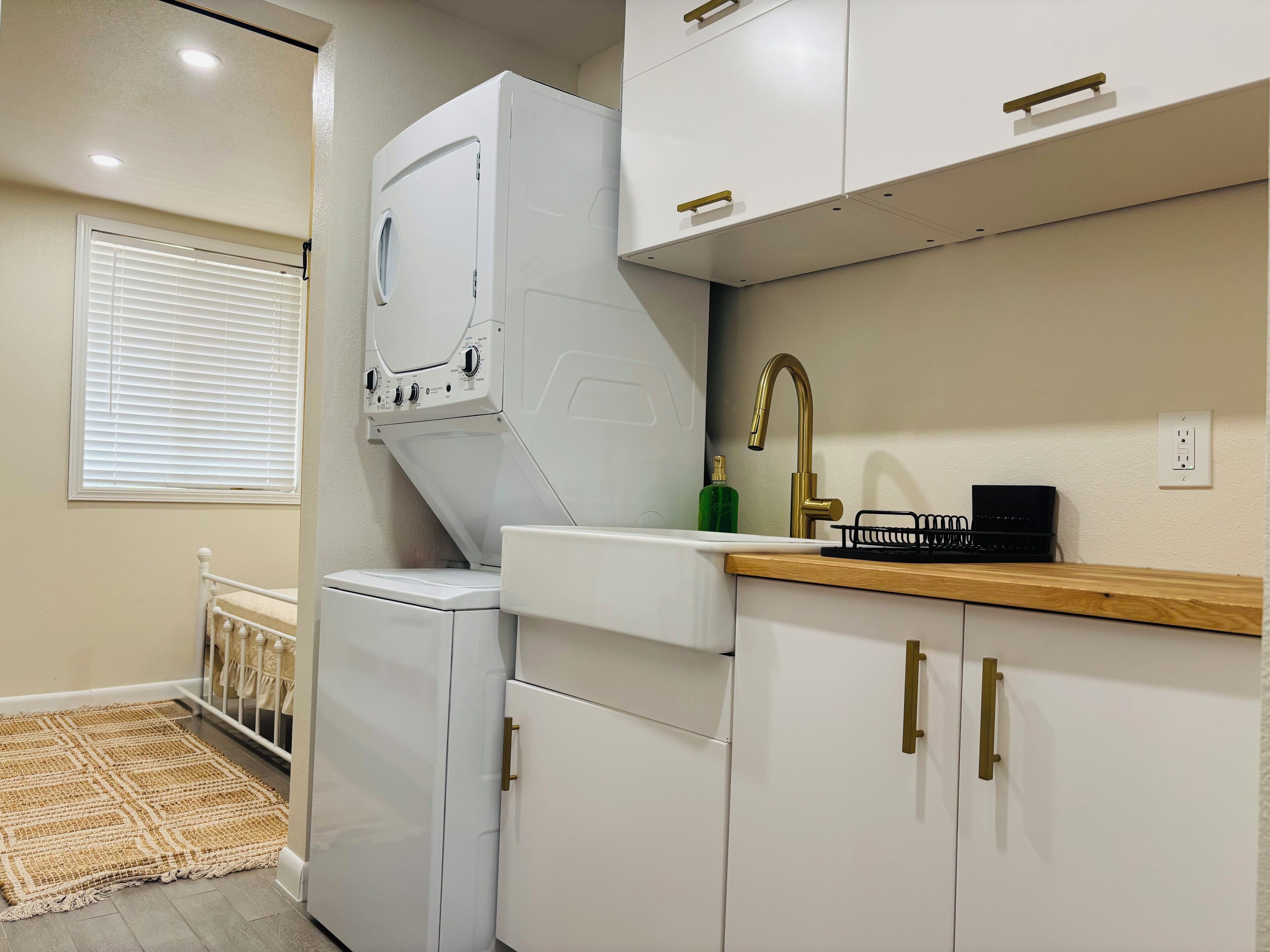 Une cuisine compacte dotée d’un lave-linge et d’un sèche-linge intégrés, d’un évier avec un robinet doré et de meubles de rangement en bois.