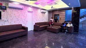 A modern lobby with dark tiled flooring, a sectional sofa, a coffee table, and a chandelier. - Hotel Om Palace (Vrindavan)