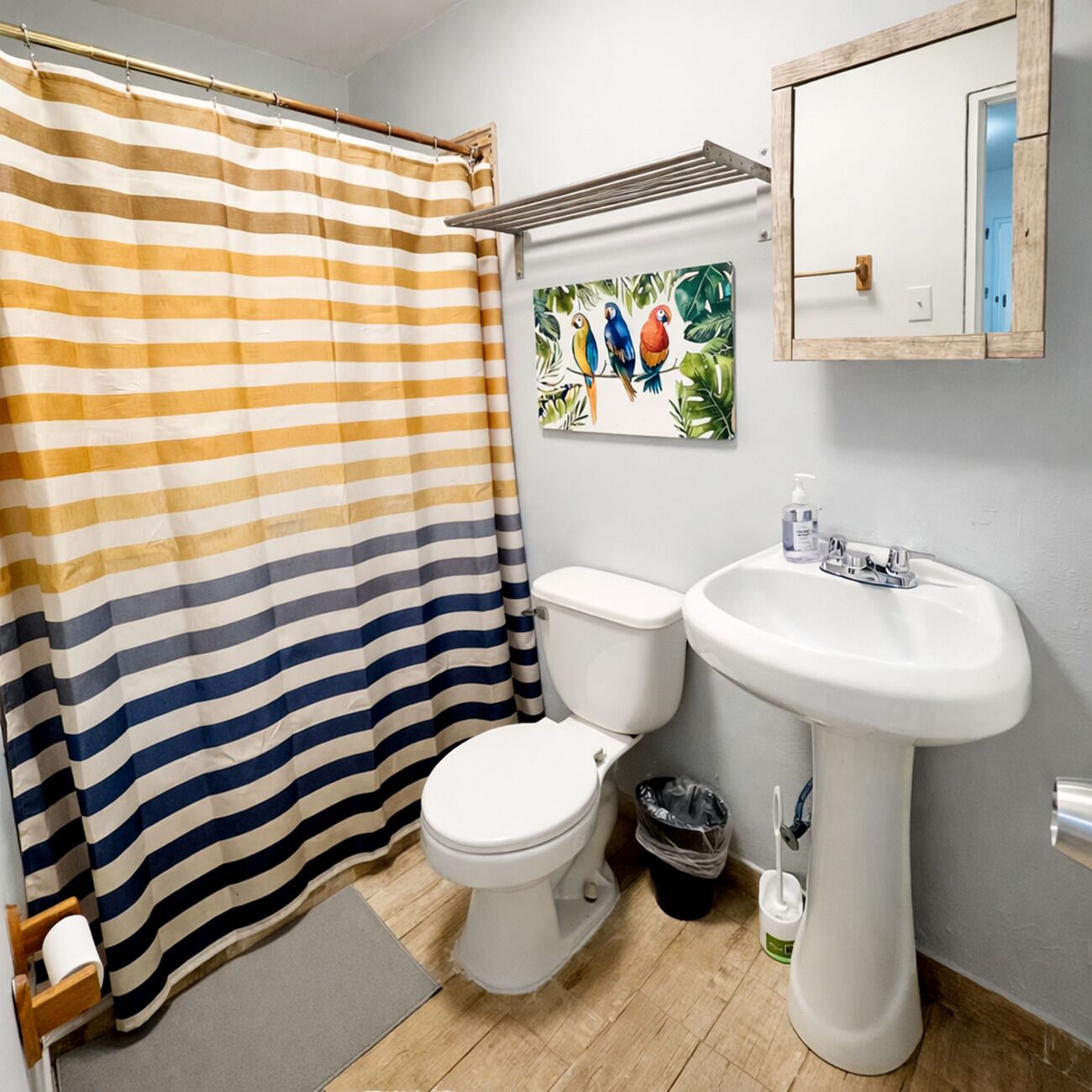 A bathroom with a striped shower curtain, a toilet, a sink, and a wall-mounted mirror.