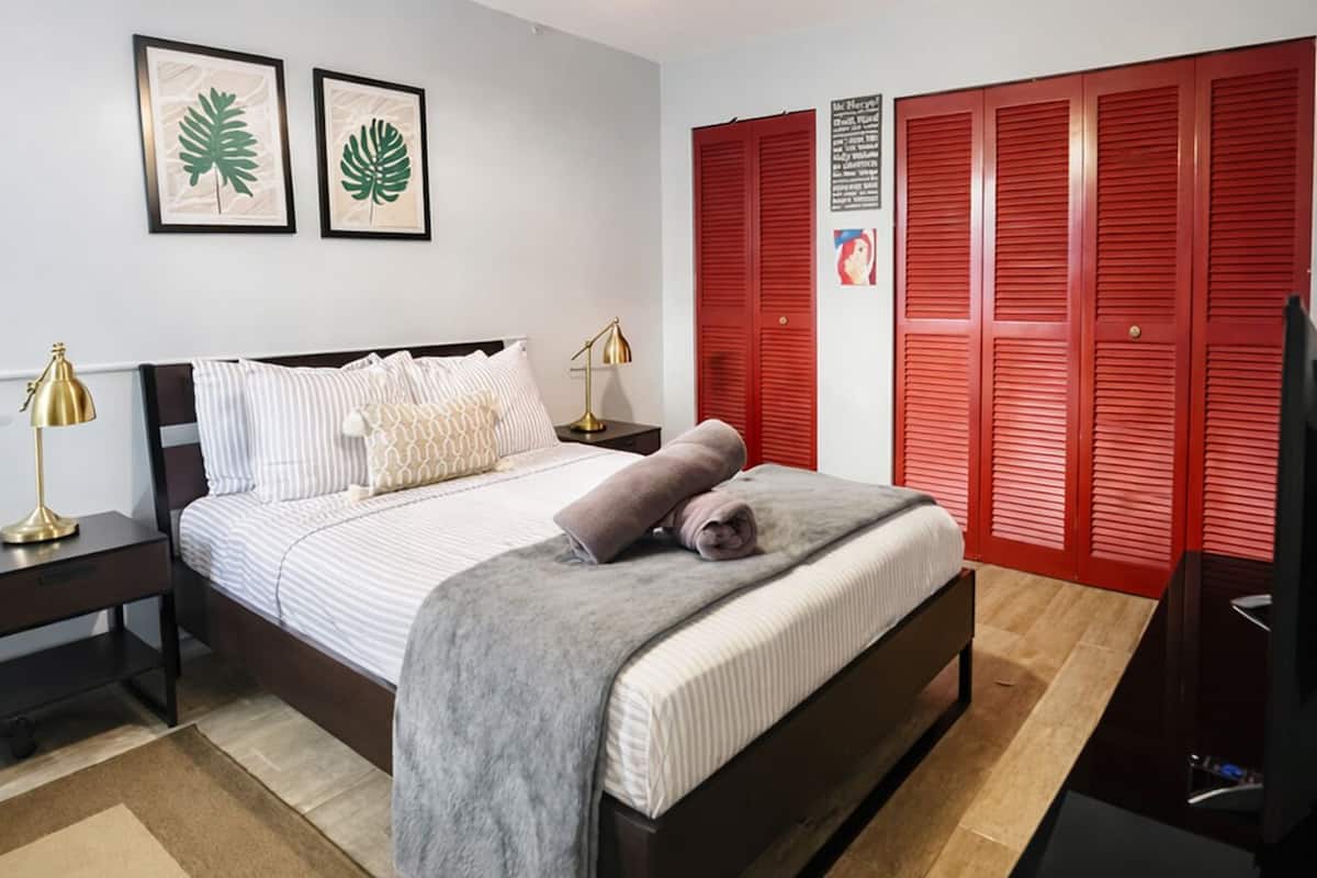 A bedroom with a bed, bedside tables, a desk, a chair, a red wardrobe, and a ceiling light.