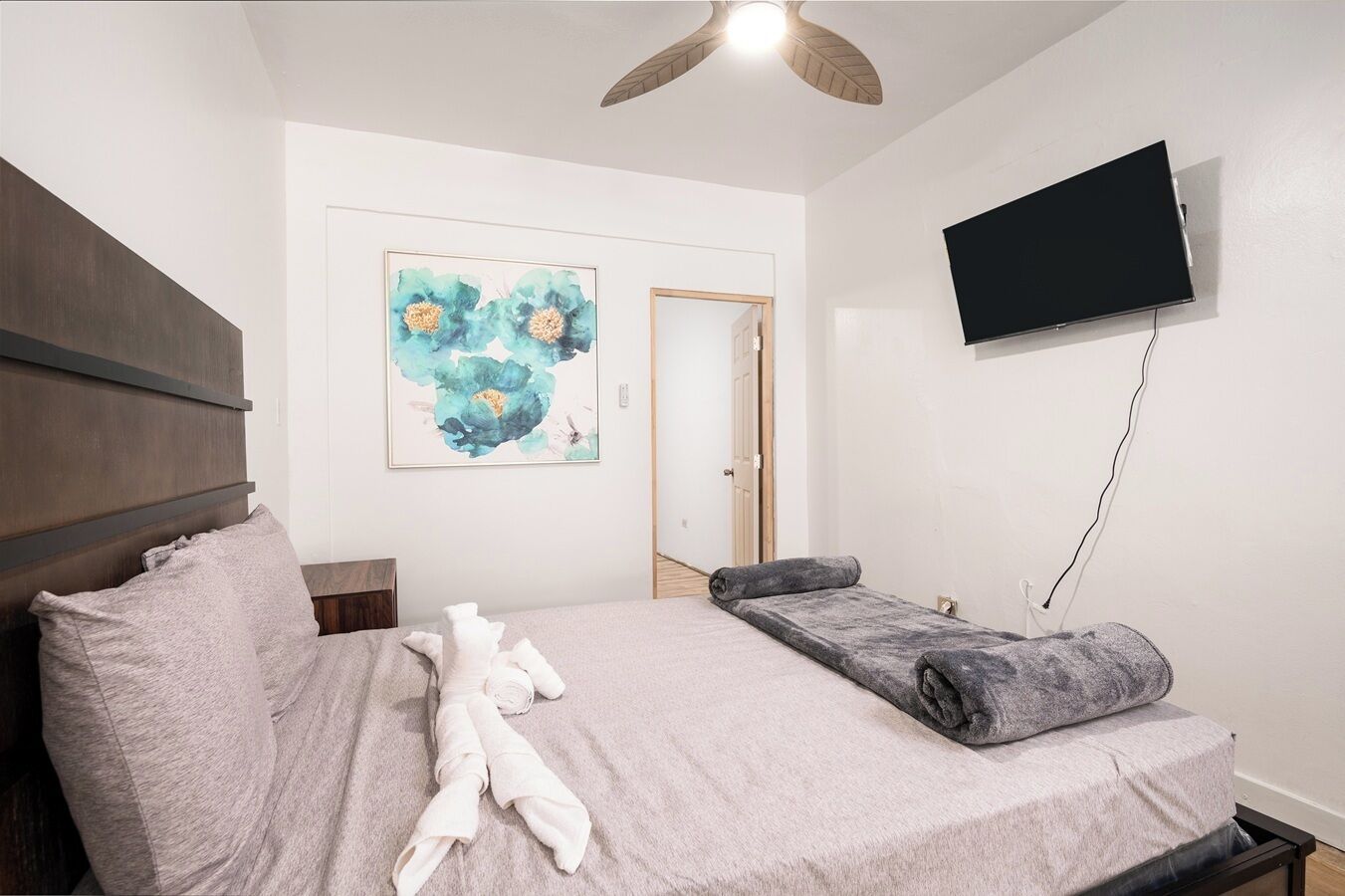 Une chambre à coucher avec un lit, un ventilateur de plafond, un téléviseur à écran plat et un tableau accroché au mur.