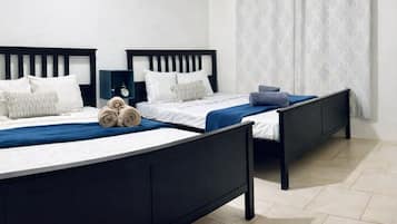 Ein Zimmer mit zwei Betten, einem Nachttisch, einer Wandklimaanlage und einem Fenster mit einem gemusterten Vorhang.