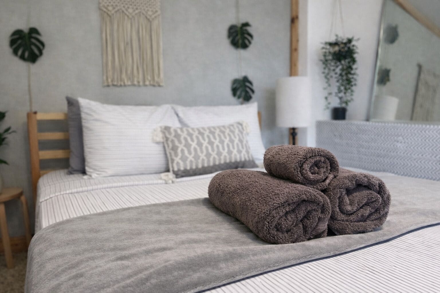 A neatly made bed with rolled towels, a bedside lamp, and a mirror.