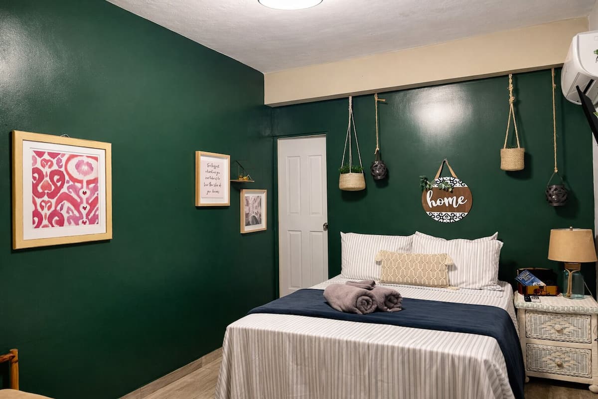 A bedroom with a bed, a bedside table, a lamp, and wall decorations including framed pictures and a sign.