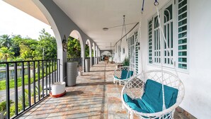 A covered balcony with white wicker chairs and a potted plant. - RainForest House (Ceiba)