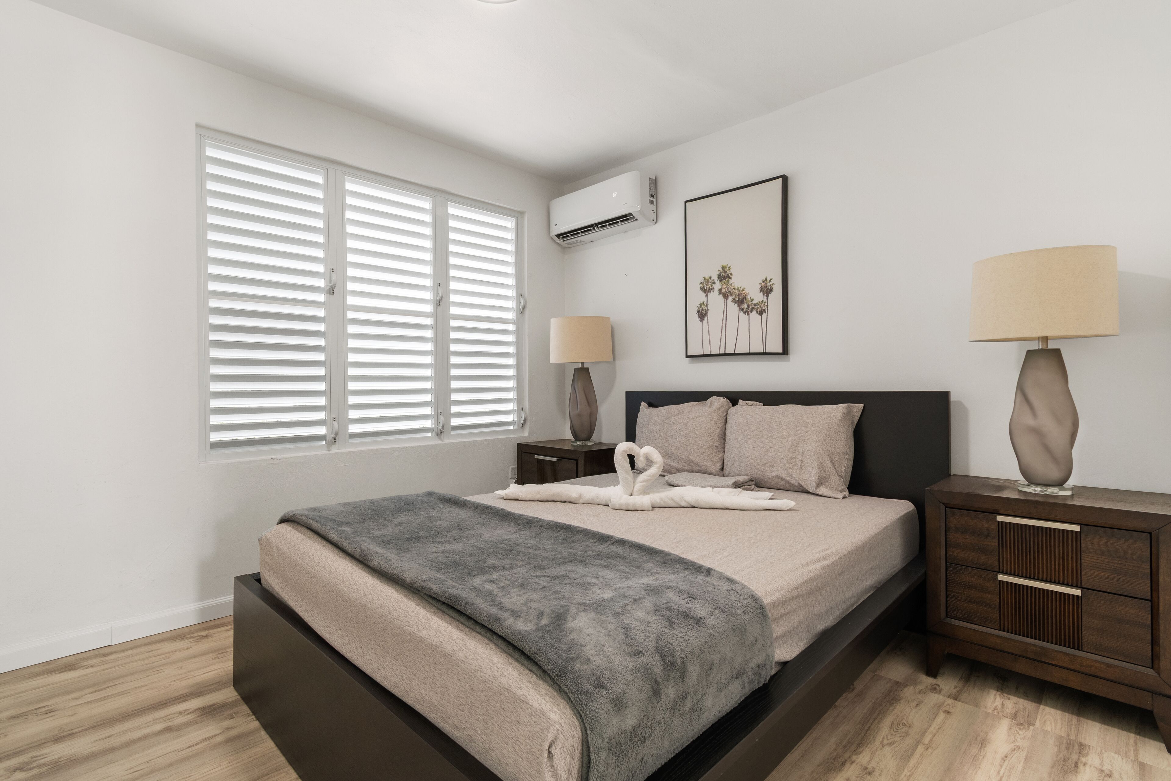 Een moderne slaapkamer met een groot bed, twee nachtkastjes, een wandairconditioner en een raam met zonwering.