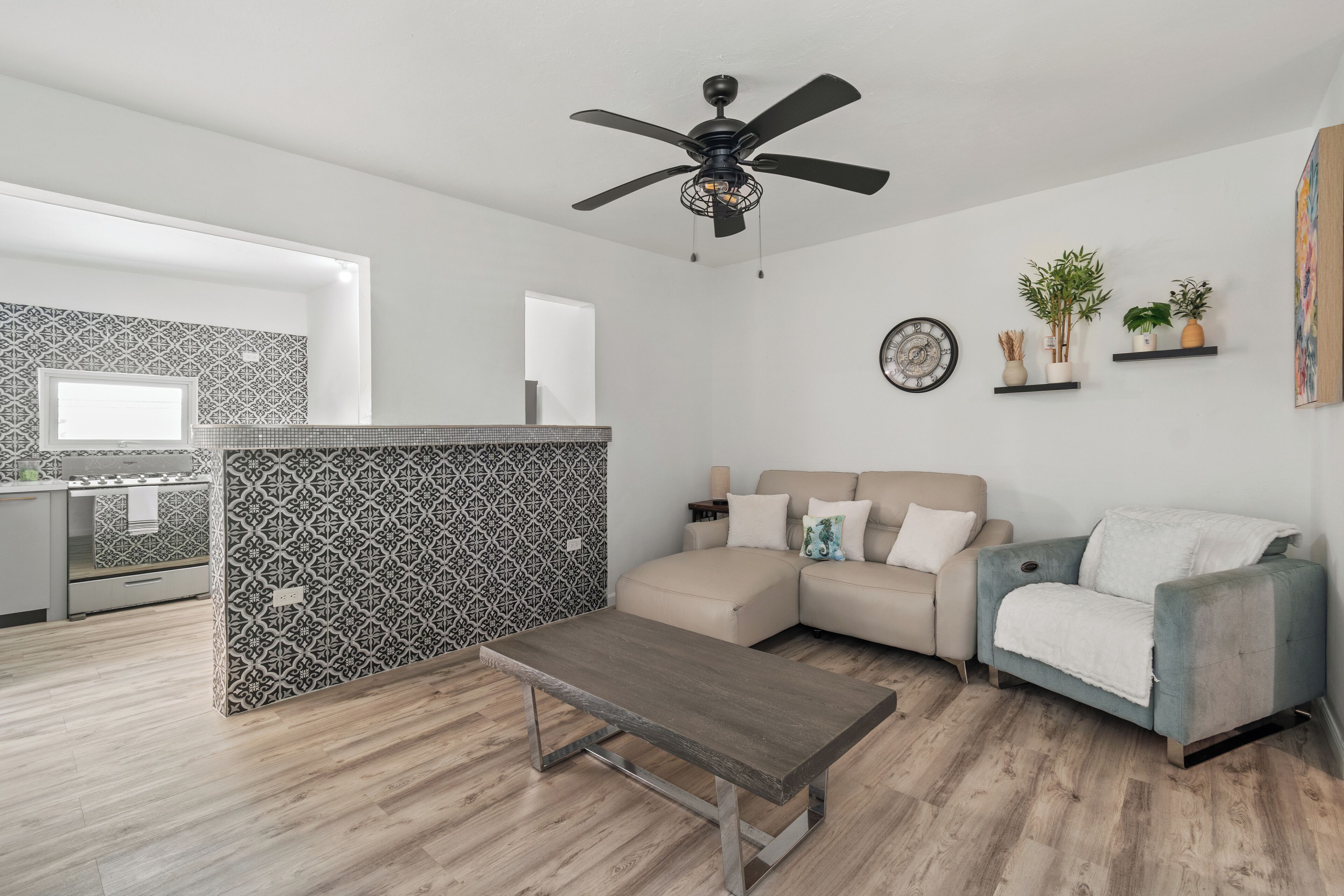 A modern living room with a sofa, a coffee table, and a kitchen area with patterned backsplash.